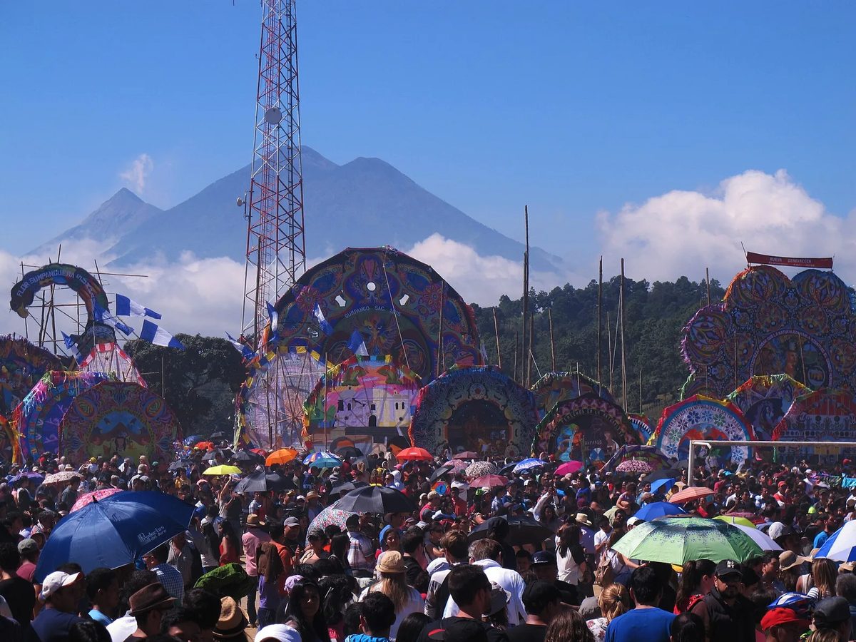 Giant kites (barriletes gigantes) over the crowd at the Sumpango festival on November 1, with a volcano in the background