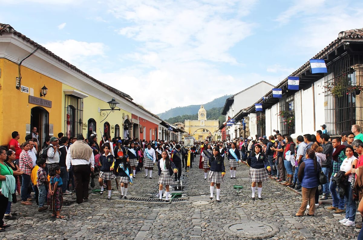School marching band parading through Antigua Guatemala on Independence Day, with Guatemalan flags lining the street