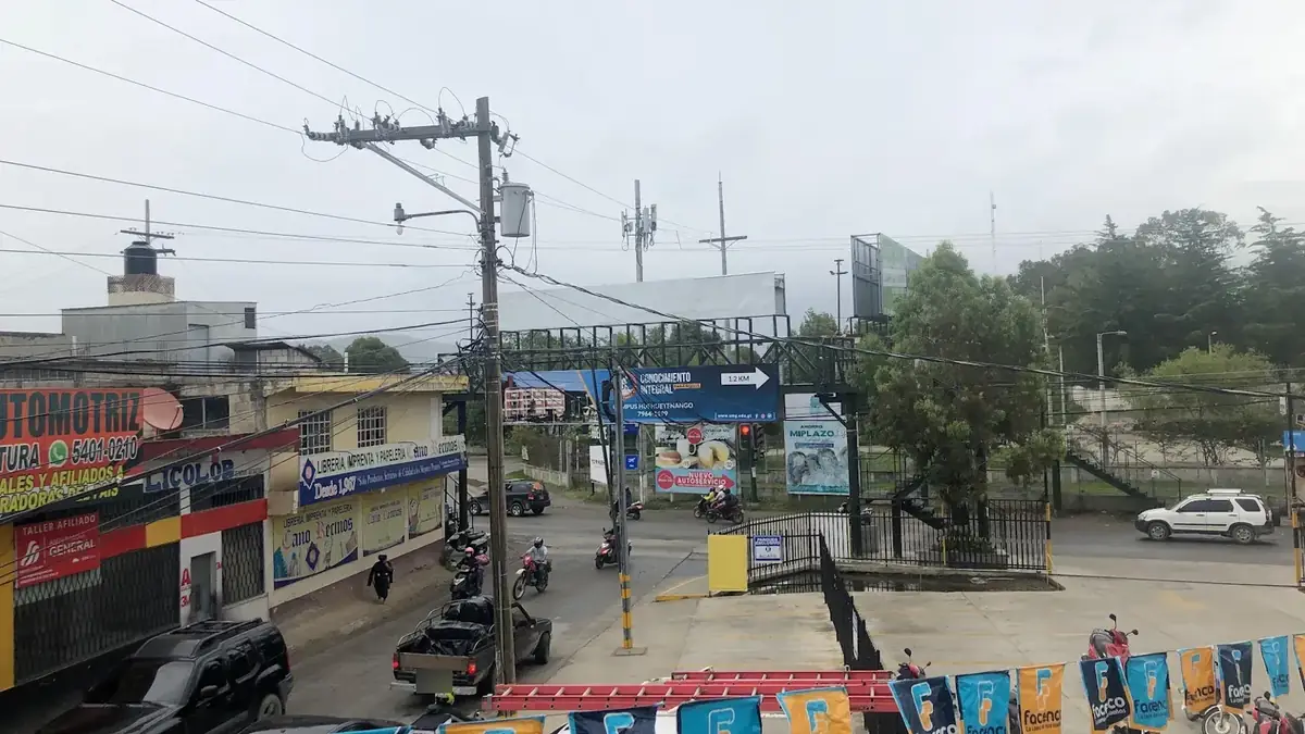Cruce concurrido con comercios y una pasarela en la ciudad de Huehuetenango